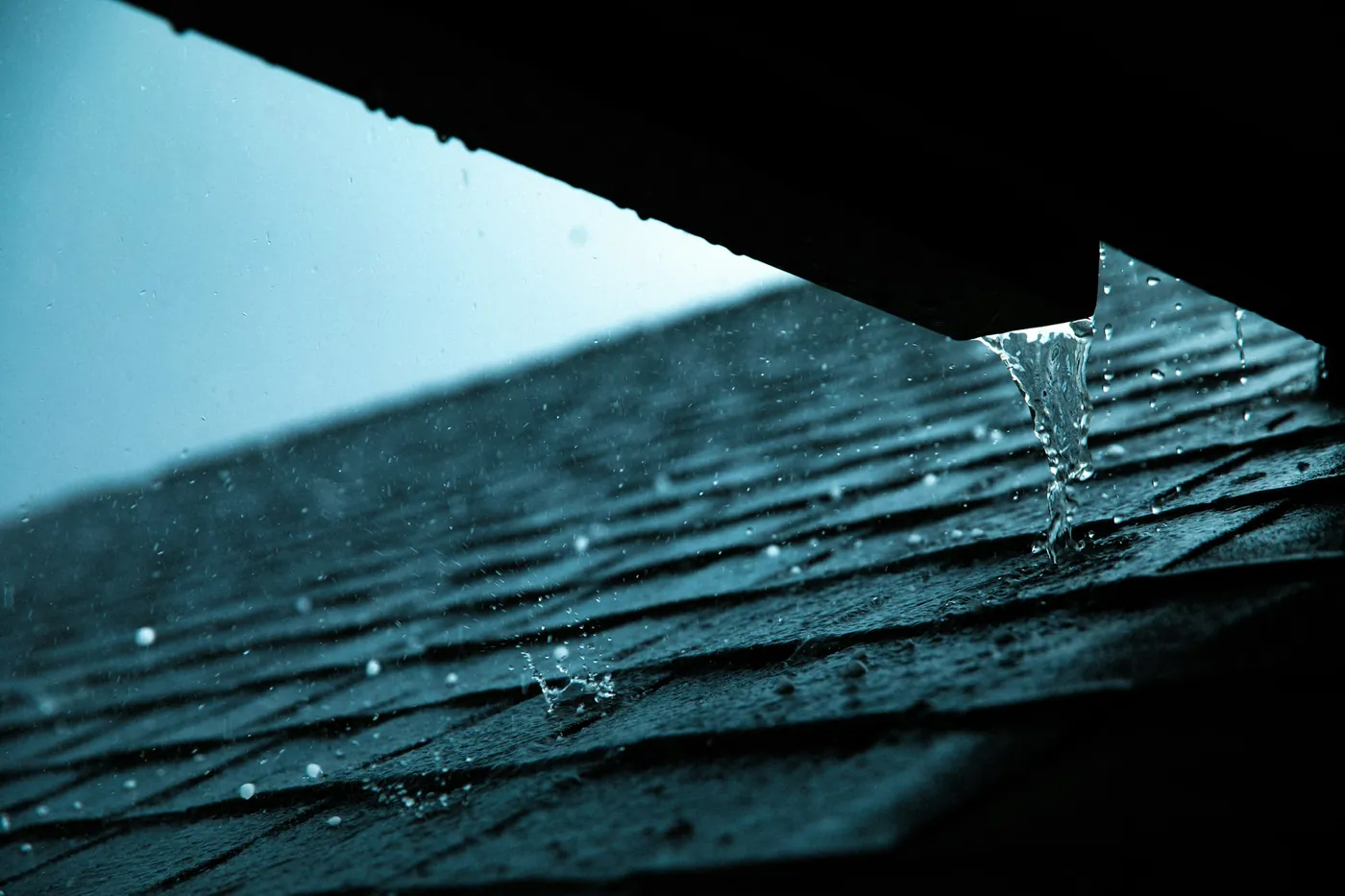 Rain running off an asphalt shingle roof during a storm