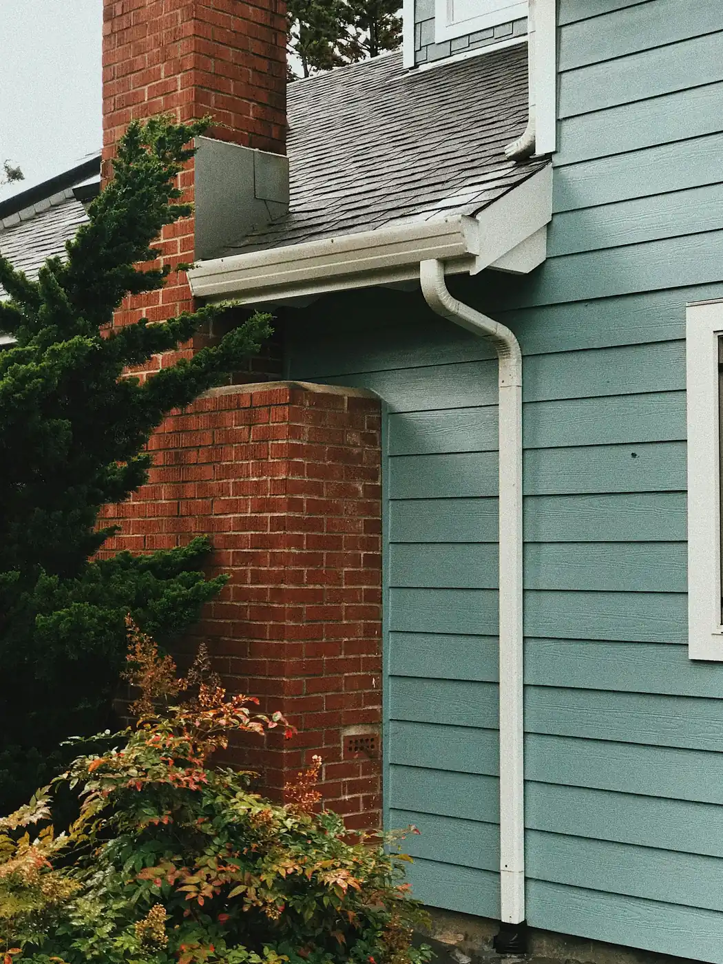 White seamless gutter and downspout beside a brick chimney